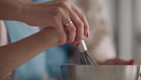 mother-and-daughter-are-cooking-in-home-closeup-of-hands-of-woman-and-little-girl-mixing-dough-by-whisk
